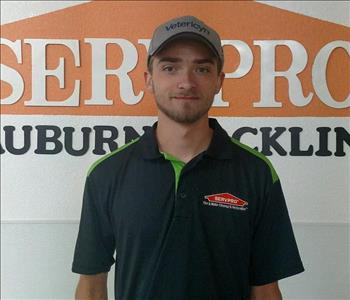 Male employee wearing a black SERVPRO shirt standing in front of a SERVPRO sign