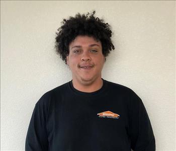 Male employee with curly hair smiling in front of a white background